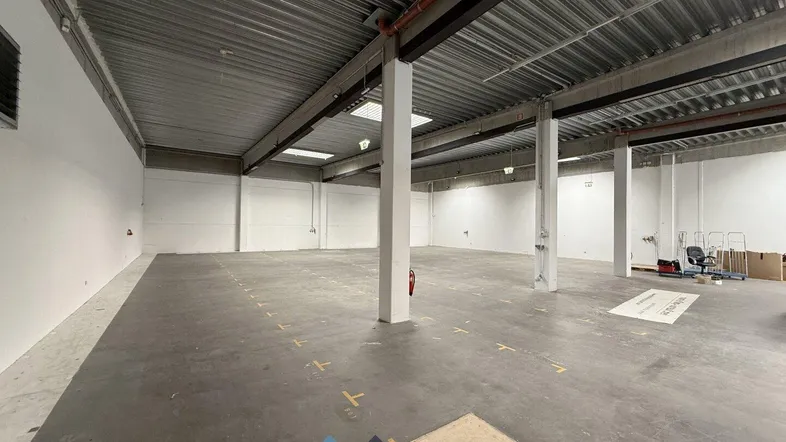 Geräumige Lagerhalle mit hohen Decken, Betonboden und natürlichem Lichteinfall durch Oberlichter.