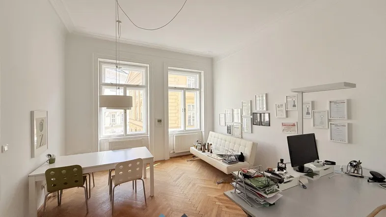 Geräumiges Büro mit Fischgrätparkett, hohen Decken und großen Fenstern, die viel Tageslicht hereinlassen.