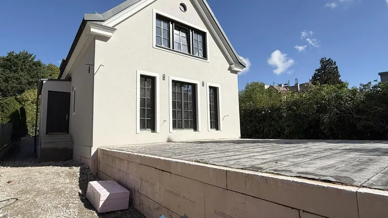 Hausfassade im Bau mit sichtbarer Isolierung und Fundament bei sonnigem Wetter.