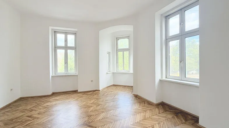 Helles Zimmer mit Fischgrätparkettboden und hohen Fenstern, ideal für Wohn- oder Schlafbereich.
