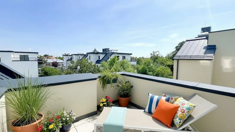 Geräumige Dachterrasse mit Sonnenliege, bunten Kissen und Blick auf die umliegenden Häuser.