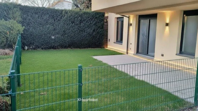 Gepflegter Gartenbereich mit Rasenfläche und gepflasterter Terrasse neben dem modernen Neubau.