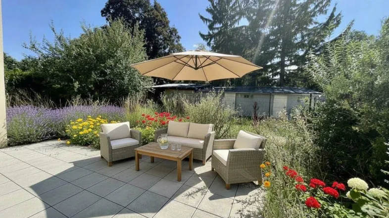 Gepflasterte Terrasse mit bequemen Gartenmöbeln, Sonnenschirm und blühenden Pflanzen.