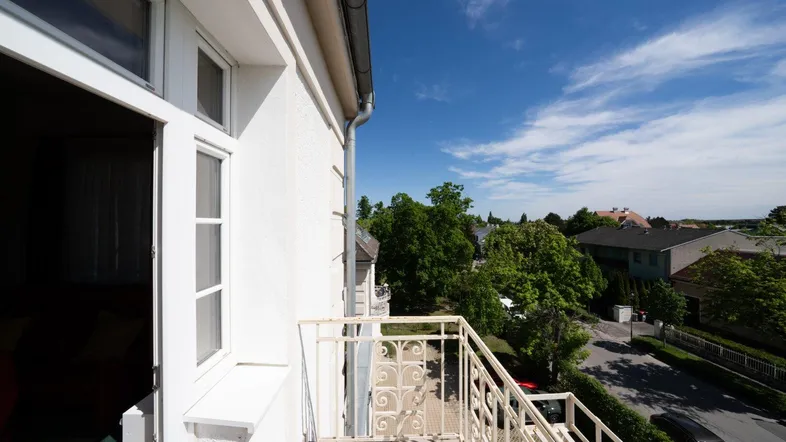 Heller Balkon mit schmiedeeisernem Geländer und Blick auf die grüne Umgebung unter blauem Himmel.