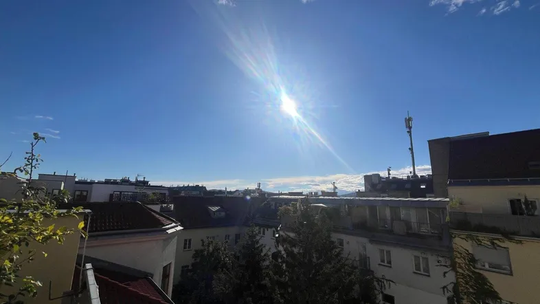Sonnige Aussicht über die Dächer der Stadt mit blauem Himmel und fernen Bergen.