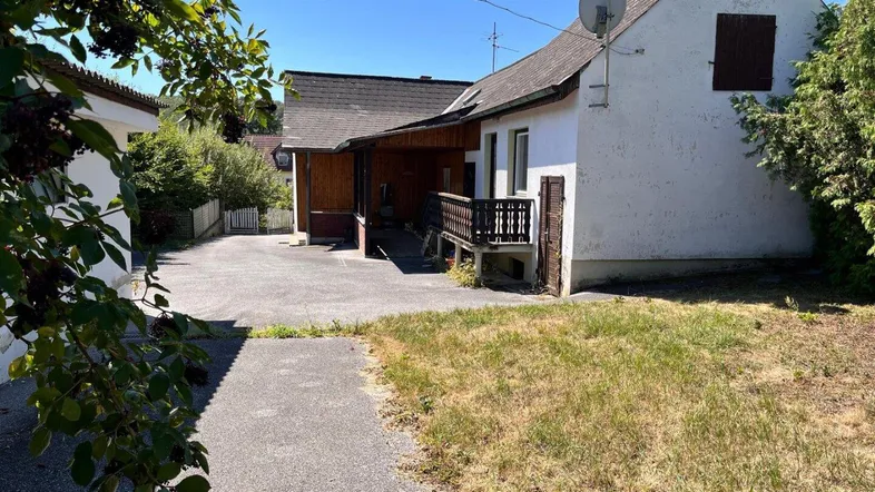 Außenansicht eines Hauses mit überdachtem Eingangsbereich, Zufahrt und trockenem Rasen.