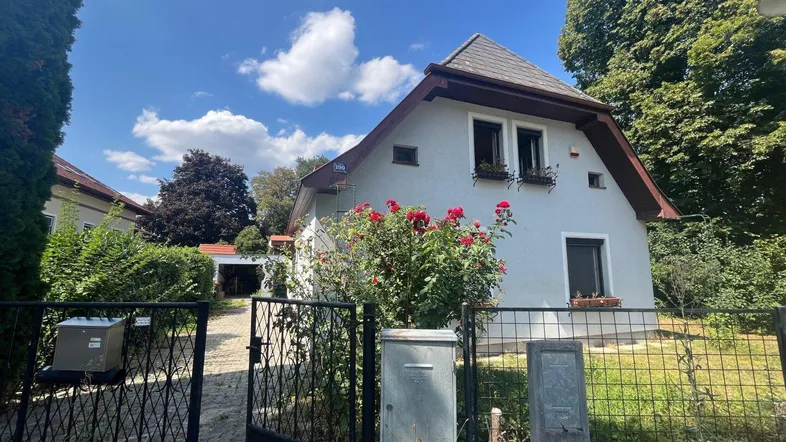 Vorderansicht des Hauses mit gepflegtem Vorgarten, Rosenbüschen und einem Eingangstor.