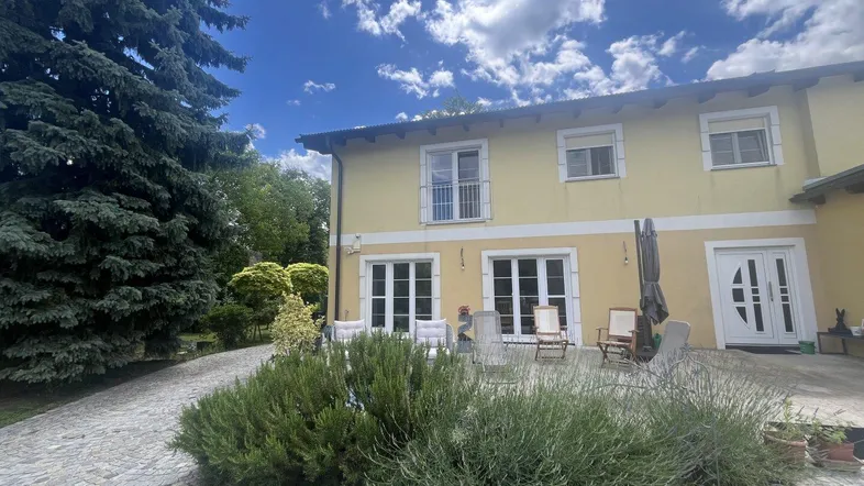Geräumige Terrasse vor dem Haus mit Sitzgelegenheiten und Blick ins Grüne unter blauem Himmel.