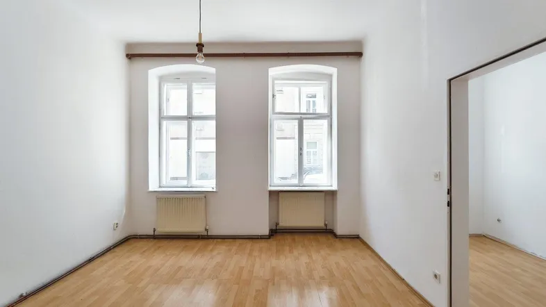 Helles, leeres Zimmer mit Parkettboden und zwei Fenstern, bereit zur individuellen Gestaltung.