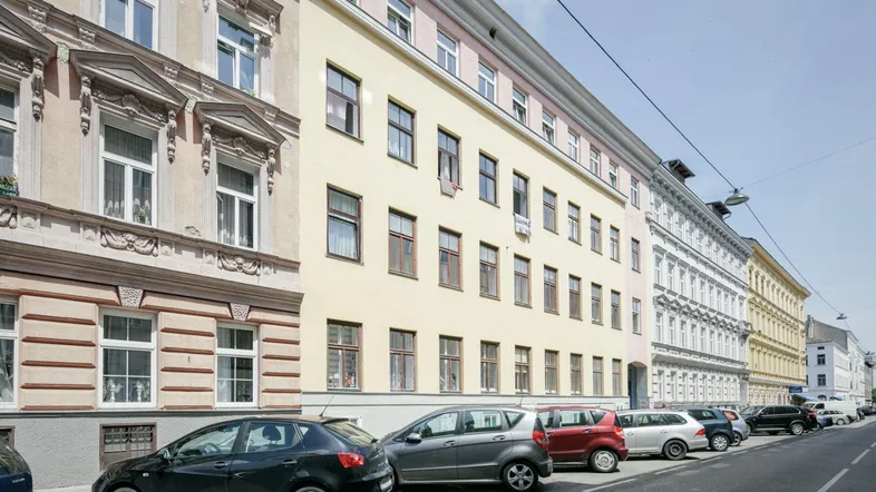 Eine belebte Straße mit parkenden Autos vor einer Reihe von Mehrfamilienhäusern in der Stadt.