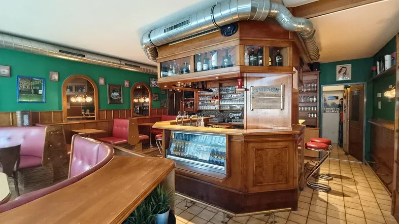 Gemütliche Bar mit traditioneller Holzeinrichtung, grünen Wänden und bequemen roten Sitzbänken, ideal für gesellige Abende.