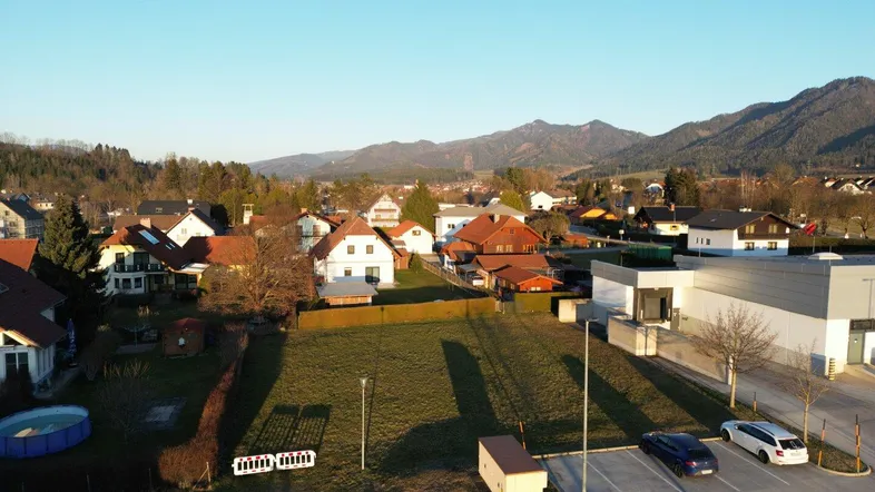 Luftaufnahme eines Baugrundstücks in einer Wohngegend mit Bergpanorama im Hintergrund.