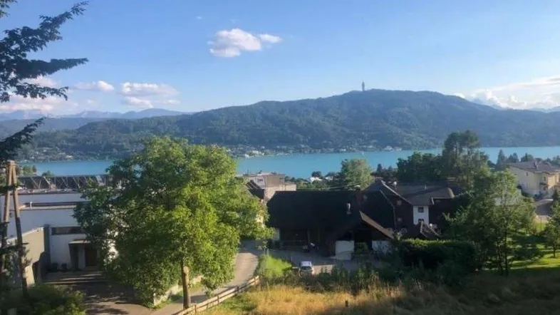 Panoramablick auf einen malerischen See und die umliegenden Berge mit vereinzelten Häusern im Vordergrund.