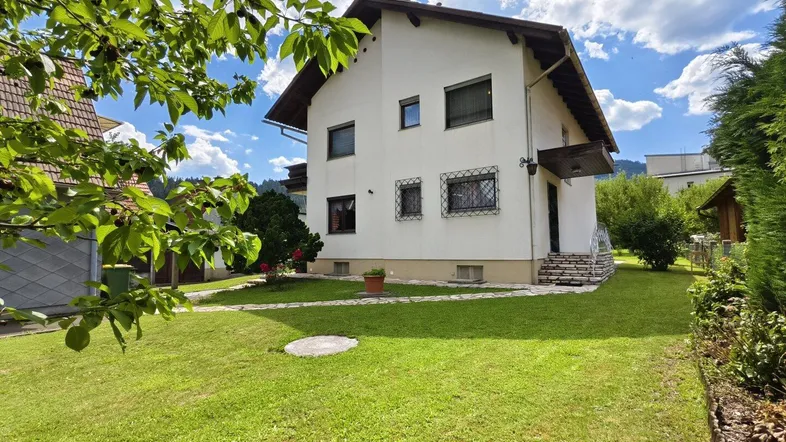 Seitliche Ansicht des Hauses mit gepflegtem Rasen und grüner Bepflanzung.
