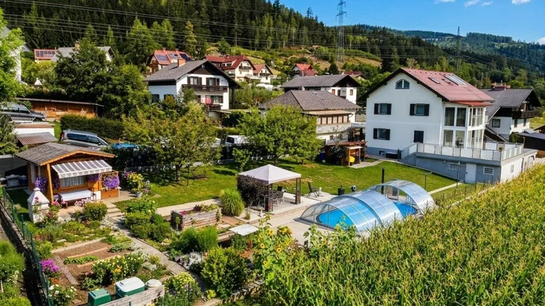 Luftaufnahme eines Wohngebiets mit mehreren Häusern, großem Garten, Pool und umliegender Naturlandschaft.