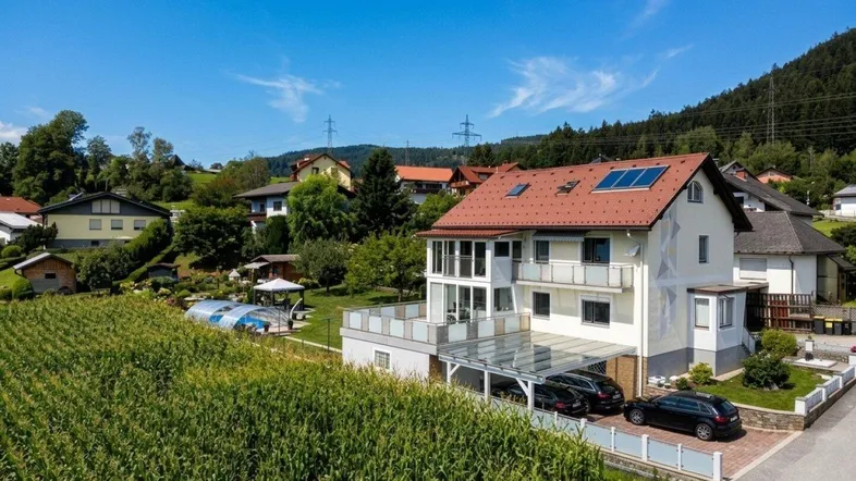 Ansicht des modernen Wohnhauses mit Carport und Poolbereich, eingebettet in eine ländliche Umgebung mit Feldern.