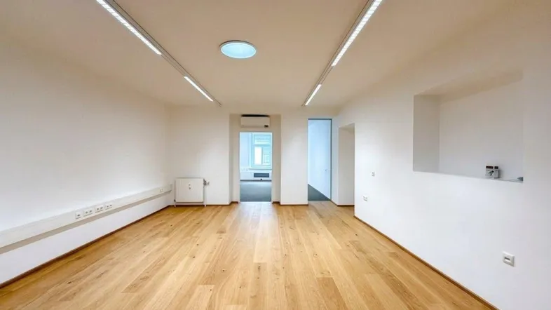 Heller Büroraum mit modernem Holzparkettboden, weißen Wänden und effizienter Deckenbeleuchtung.