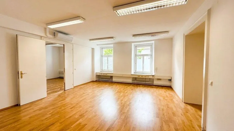 Heller, leerer Raum mit Holzboden und zwei Fenstern, ideal für Büro oder Wohnbereich.