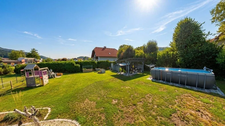Sonniger Garten mit großem Aufstellpool, Spielplatz und viel Grünfläche für Freizeitaktivitäten.