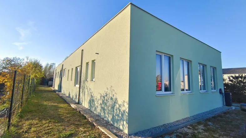 Seitenansicht des Gebäudes mit hellgrüner Fassade, vielen Fenstern und einem Kiesweg entlang der Seite.
