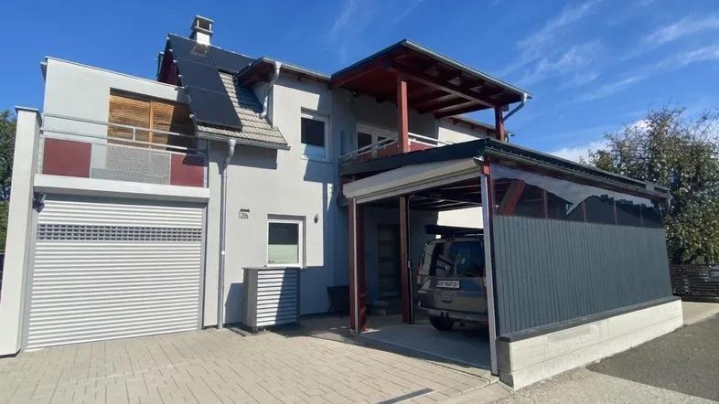 Modernes Einfamilienhaus mit integrierter Garage, Carport und Photovoltaikanlage unter blauem Himmel.