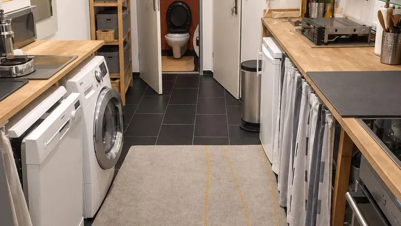 Funktionale Küche mit Holz-Arbeitsplatten, Waschmaschine und Blick in ein separates Gäste-WC.