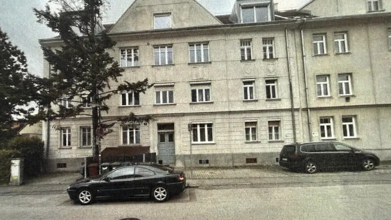 Klassisches Mehrfamilienhaus mit mehreren Etagen und parkenden Autos auf der Straße.