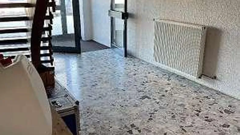 Eingangsbereich mit Treppe, Terrazzoboden und Heizkörper, der zu den oberen Etagen führt.