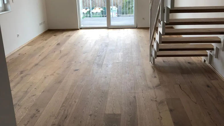 Helles Wohnzimmer mit neuem Holzboden, offener Treppe und Zugang zu einem Balkon.