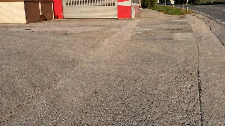 Eine rote Industriehalle mit einem großen Rolltor und einem asphaltierten Vorplatz unter blauem Himmel.