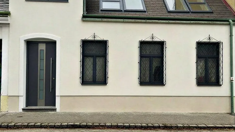 Die helle Fassade des Hauses mit Eingangstür und Dachfenstern zur Straße hin.