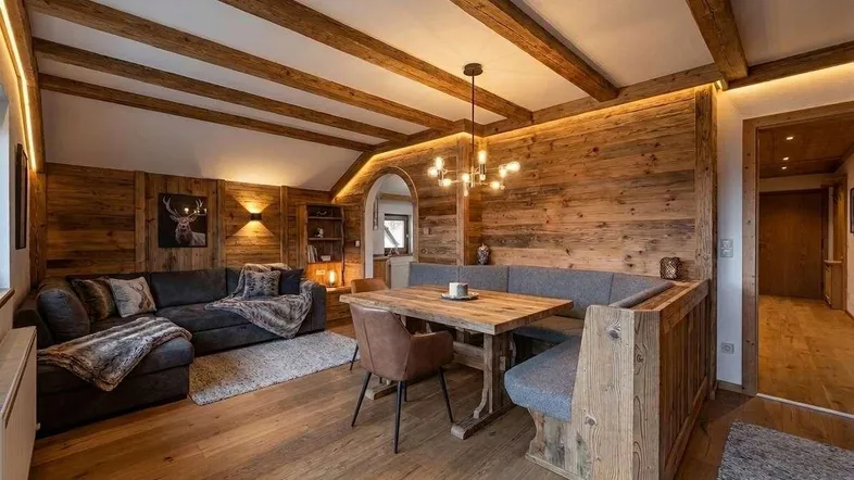Gemütlicher Wohn-Essbereich im alpinen Stil mit Holzbalken, Holzwänden und bequemer Sitzecke.