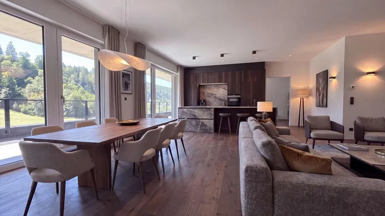 Helles, offenes Wohn-Esszimmer mit moderner Küche, Holzboden und Bergblick durch große Fenster.