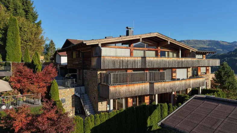 Großes Holzchalet mit mehreren Balkonen und Terrassen in alpiner Umgebung unter blauem Himmel.