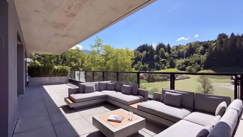 Große moderne Terrasse mit bequemen Lounge-Möbeln und weitem Blick ins Grüne unter blauem Himmel.