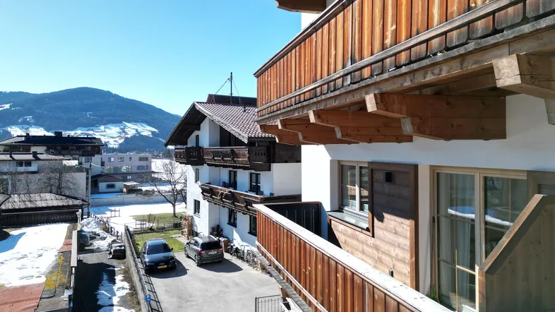 Blick von einem Balkon auf die Straße, benachbarte Gebäude und die schneebedeckten Berge.