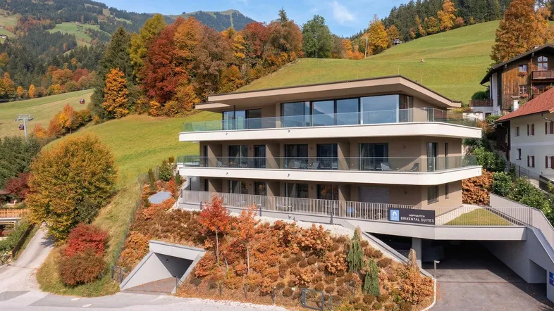 Modernes Apartmentgebäude mit begrüntem Dach und Balkonen in alpiner Hanglage.