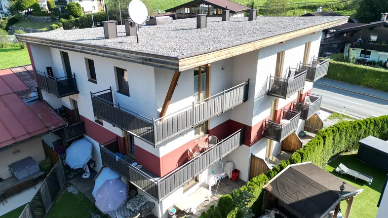 Mehrfamilienhaus mit Balkonen, Gartenbereich und Blick auf die umliegende Berglandschaft.