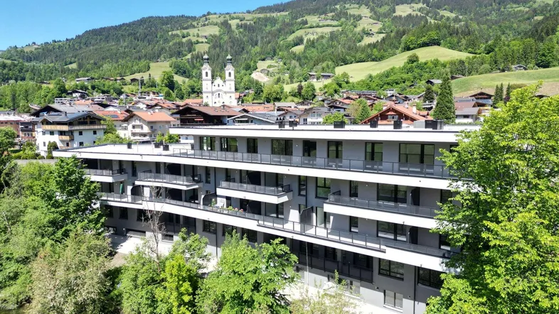 Gebäude am Flussufer mit Balkonen und Blick auf das Dorf und die Berge.