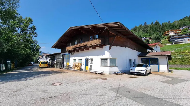 Gebäudeansicht mit traditioneller Holzverkleidung und großem Parkplatz vor einer Bergkulisse.