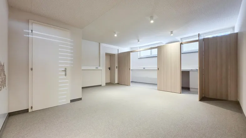 Geräumiger Büroraum mit Teppichboden, hellen Wänden und flexiblen Trennwänden für verschiedene Arbeitsbereiche.