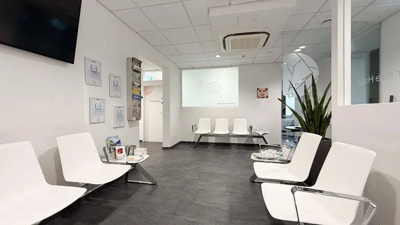 Heller und moderner Wartebereich mit bequemen Sitzgelegenheiten und einem Bildschirm.