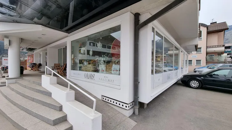 Außenansicht eines modernen Geschäftsgebäudes mit großen Schaufenstern, Treppen und einer Rampe für Barrierefreiheit.