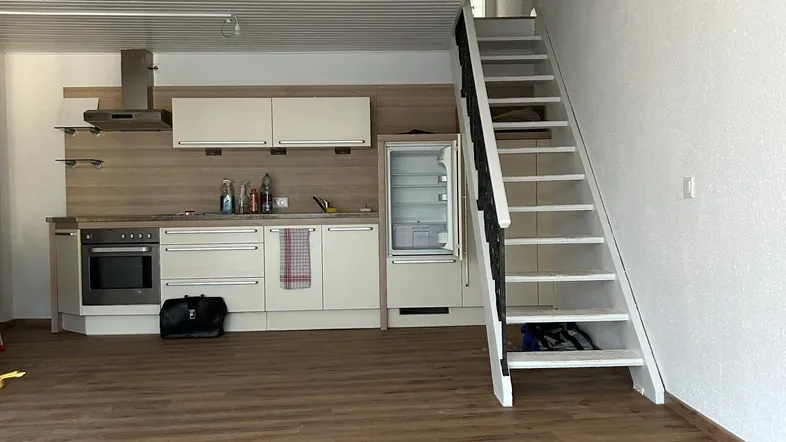 Offener Wohnbereich mit integrierter Küche, Laminatboden und einer Treppe zum Obergeschoss.
