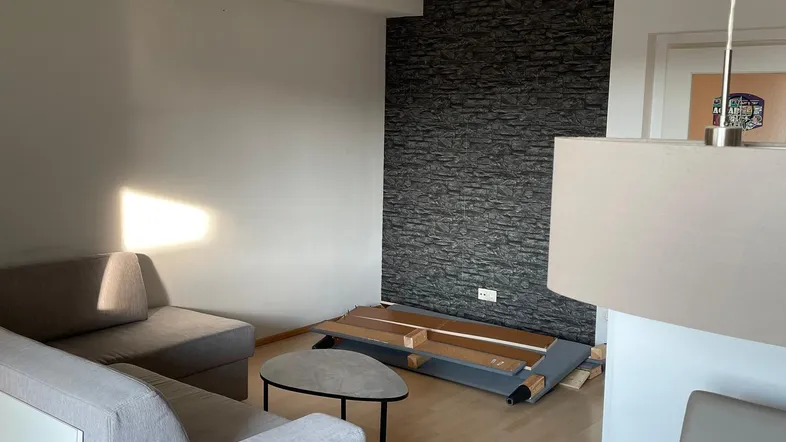 Helles Wohnzimmer mit beiger Couch, Couchtisch und einer dunklen Akzentwand.