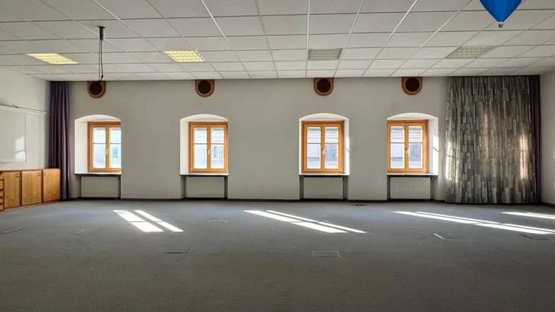 Großer, heller Raum mit Teppichboden, vielen Fenstern und abgehängter Decke, ideal für Büros oder Veranstaltungen.