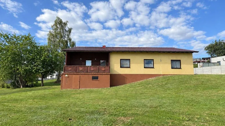 Einfamilienhaus mit gelber Fassade und braunem Sockel auf einem grünen Hügel.