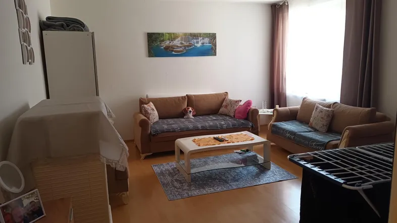 Gemütliches Wohnzimmer mit beigen Sofas, Couchtisch und hellem Laminatboden, gut beleuchtet.