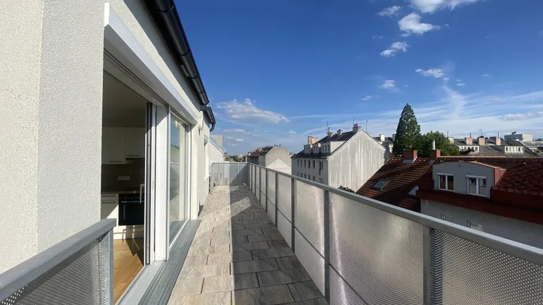 Langer, sonniger Terrassenbereich mit Fliesenboden und Blick auf die umliegenden Gebäude.