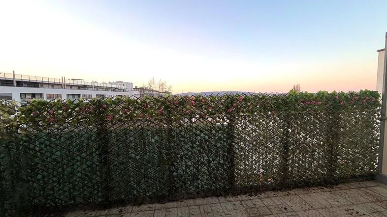 Balkon mit Fliesenboden und grüner Sichtschutzwand, bietet einen weiten Blick über die Umgebung.